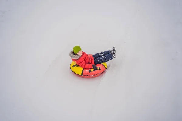 Das Kind hat Spaß auf der Schneekanone. Junge reitet auf einem Schlauch. Winterspaß für Kinder — Stockfoto