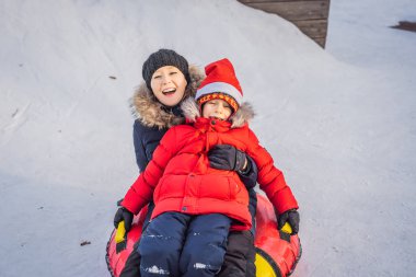 Anne oğul şişme bir kış kızağı borusuna biniyor. Tüm aile için kış eğlencesi
