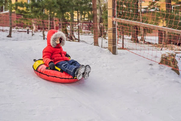 Criança se divertindo no tubo de neve. O rapaz está a montar um tubo. Diversão de inverno para crianças — Fotografia de Stock