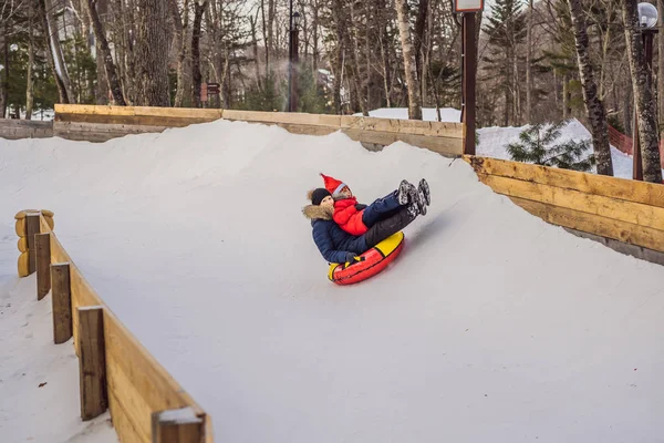 Anya fia lovagolni egy felfújható téli szánkó cső. Téli szórakozás az egész családnak — Stock Fotó