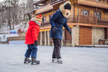 Genç bir anne, oğluna buz pateni pistinde buz pateni öğretiyor. Aile buz pateni sahasında kışın keyfini çıkarır.