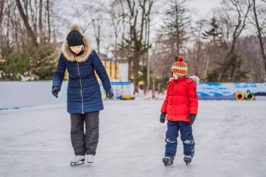 Genç bir anne, oğluna buz pateni pistinde buz pateni öğretiyor. Aile buz pateni sahasında kışın keyfini çıkarır.