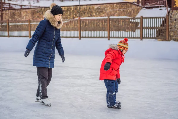 年轻的母亲在户外溜冰场教她的小儿子滑冰。家里人在户外冰场上享受冬天 — 图库照片