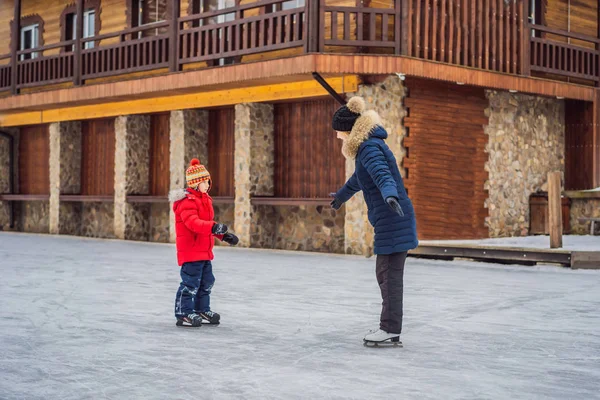 Jovem mãe ensinando seu filho patinagem no gelo no ringue de patinação ao ar livre. Família desfrutar de inverno no rinque de gelo ao ar livre — Fotografia de Stock