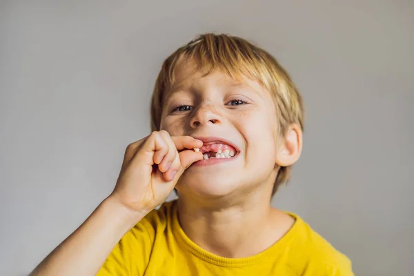 Маленький белый мальчик держит молочный зуб между пальцами и смеется, глядя в камеру. — стоковое фото