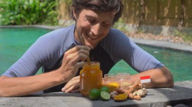 Genç bir adam yüzme havuzunda yüzen ulusal Balili Jamu içkisini içiyor.