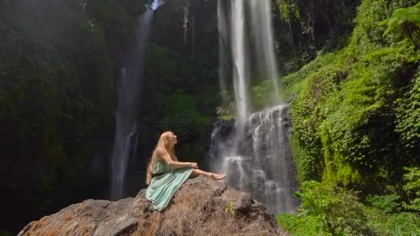 Young woman tourist visits the biggest waterfall on the Bali island - the Sekumpul waterfall. Slowmotion shot. Travel to Bali concept — Stock Video