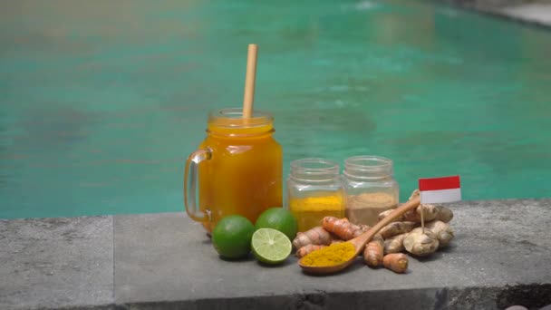 Een hand van een man neemt een glas met nationale balinese drank Jamu uit de zijkant van een zwembad — Stockvideo