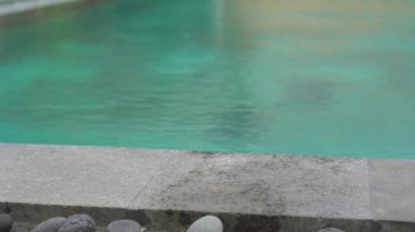 A glass with national balinese drink and its ingreedients - turmeric, jinjer and limes standing on the side of a swimming pool