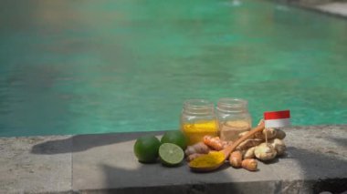 A hand of a man put a glass with national Balinese drink Jamu on the side of a swimming pool