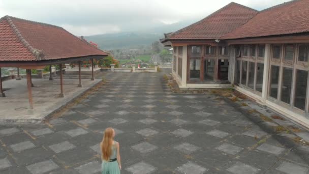 Légi felvétel egy női turistáról, aki meglátogatja az elhagyatott és titokzatos hotelt Bedugul-ban. Indonézia, Bali sziget. Bali utazási koncepció — Stock videók