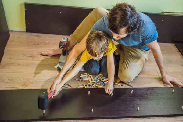 父亲和儿子组装家具。男孩帮助他的爸爸在家里。快乐家庭概念 — 图库照片