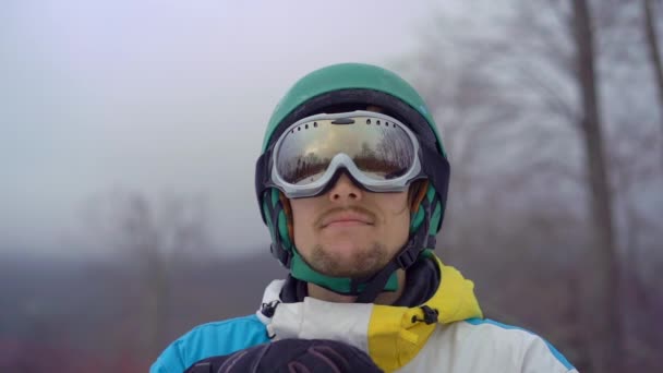 Closeup shot of a young man wearing a snow googles looks at a hillside. Winter holidays concept. Slowmotion shot — Stock Video