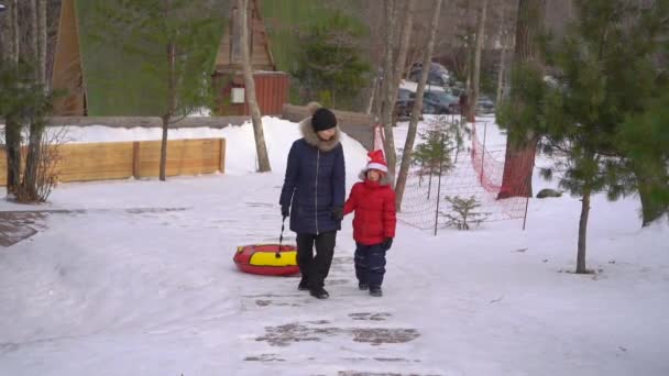 Eine junge Frau und ihr kleiner Sohn amüsieren sich beim Tubing in einem Aktivitätenpark in den Bergen. Winterferienkonzept — Stockvideo