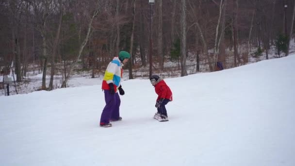 若い男のスノーボードインストラクターは小さな男の子にスノーボードに乗る方法を教えます。冬の活動の概念。スローモーションショット — ストック動画