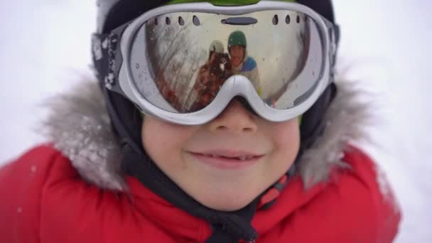 Mam en pap worden weerspiegeld in de jongensskibril. Mam en pap leren een jongen skiën of snowboarden. Wintervakantie concept. Langzame schot. — Stockvideo