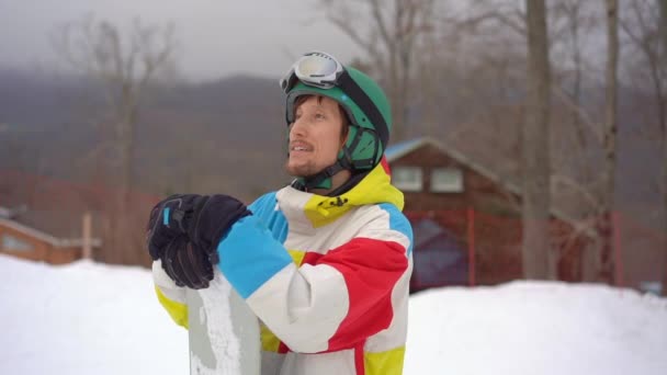 Primer plano de un joven que llevaba un casco con una tabla de snowboard en un resort de montaña. Concepto de vacaciones de invierno. Disparo en cámara lenta — Vídeo de stock