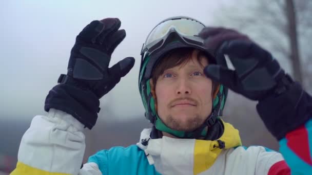 Nahaufnahme eines jungen Mannes mit Helm und Snowboard in einem Bergresort. setzt er seine Schneebrille auf. Winterferienkonzept. Zeitlupenschuss — Stockvideo