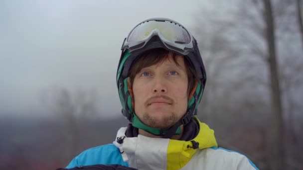 Крупный план молодого человека в шлеме со сноубордом на горном курорте. Он выкладывает свои снежные гуглы. Концепция зимнего отдыха. Слоумоушн — стоковое видео