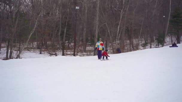若い男のスノーボードインストラクターは小さな男の子にスノーボードに乗る方法を教えます。冬の活動の概念。スローモーションショット — ストック動画