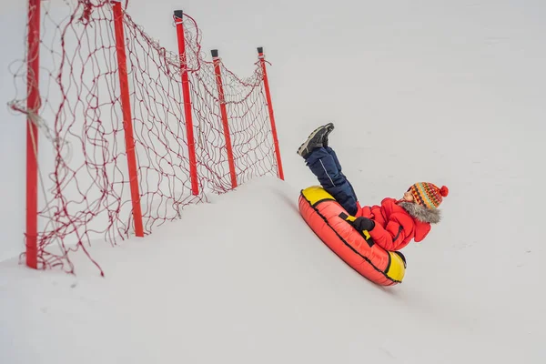 Criança se divertindo no tubo de neve. O rapaz está a montar um tubo. Diversão de inverno para crianças — Fotografia de Stock