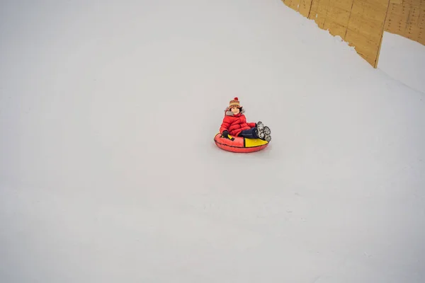 Das Kind hat Spaß auf der Schneekanone. Junge reitet auf einem Schlauch. Winterspaß für Kinder — Stockfoto