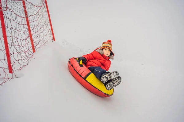 Criança se divertindo no tubo de neve. O rapaz está a montar um tubo. Diversão de inverno para crianças — Fotografia de Stock