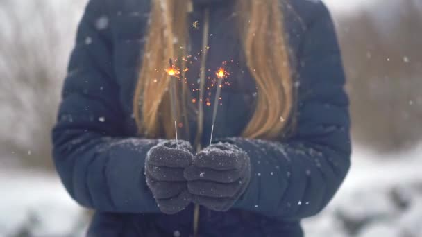 Γυναίκα κρατά μια σπίθα ή Bengal φώτα στα χέρια της σε ένα χιονισμένο φόντο — Αρχείο Βίντεο