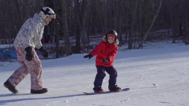 A fiatalember snowboard oktató megcsiklandozza a kisfiút, hogyan kell snowboardozni. Téli tevékenységek koncepciója — Stock videók