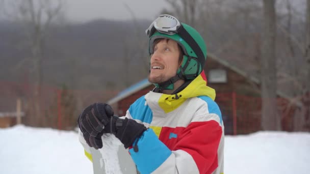 Közelkép egy fiatalemberről, aki sisakot visel egy snowboarddal egy hegyi üdülőhelyen. Téli ünnepek koncepciója. Lassított felvétel — Stock videók