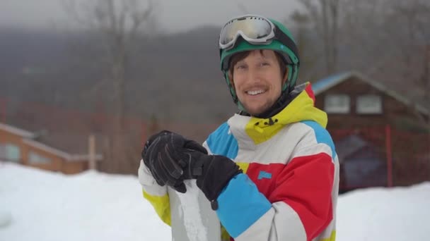 Närbild bild av en ung man klädd i hjälm med snowboard i en bergsort. Begreppet vinterlov. Slowmotion skott — Stockvideo