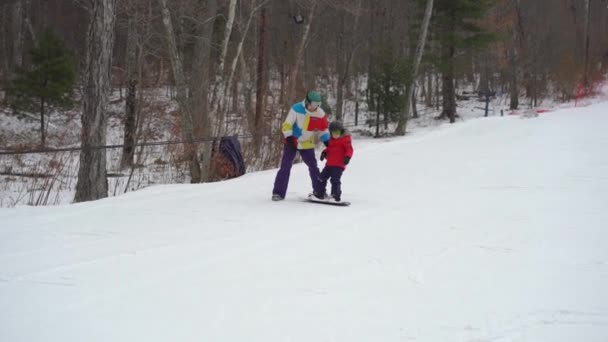 A fiatalember snowboard oktató megcsiklandozza a kisfiút, hogyan kell snowboardozni. Téli tevékenységek koncepciója — Stock videók