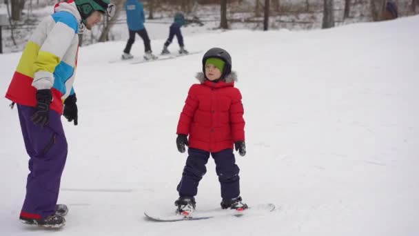 Il giovane istruttore di snowboard solletica il bambino come cavalcare uno snowboard. Concetto attività invernali — Video Stock