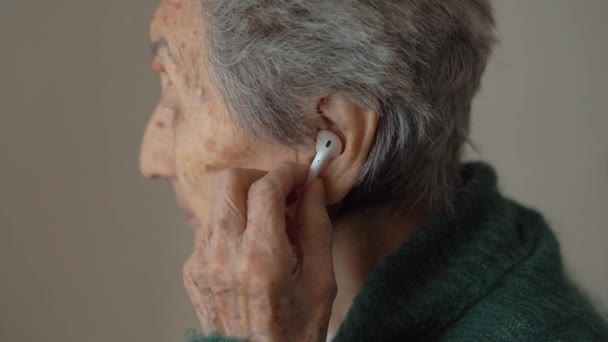 Old woman uses wireless earphones. Old person and technologies — ストック動画