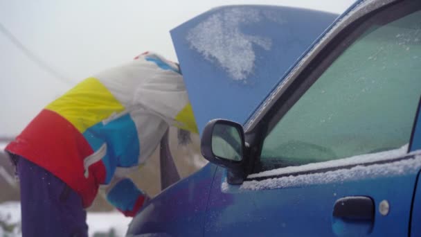 Winter, falling snow. Man on the road have troubles with his car. He is trying to find problem with an engine — ストック動画