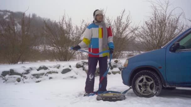 Зима, выпадает снег. У человека на дороге проблемы с машиной. Он ждет, когда кто-нибудь возьмет машину на буксир. — стоковое видео