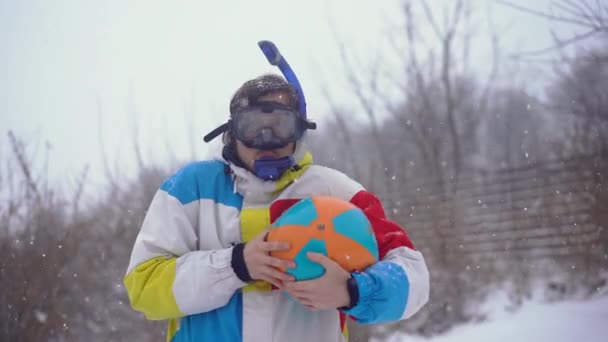 Grappige man met een duikmasker met een opblaasbare bal staat onder een sneeuwval. Verloren in de tijd — Stockvideo