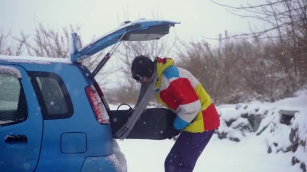 Молодой человек пытается поместить свой сноуборд в маленькую машину, но он не может. Концепция недостаточного пространства в автомобиле — стоковое видео
