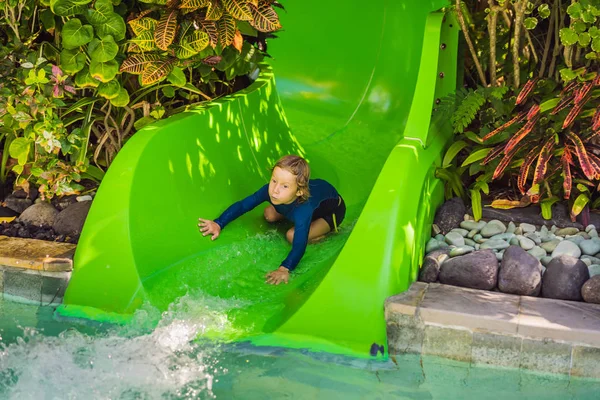 Menino feliz no slide de água em uma piscina se divertindo durante as férias de verão em um belo resort tropical — Fotografia de Stock