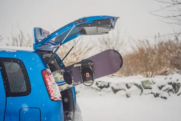 The snowboard does not fit into the car. A snowboarder is trying to stick a snowboard into a car. Humor, fun — Stock Photo, Image