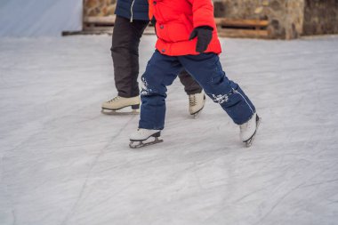 Genç bir anne, oğluna buz pateni pistinde buz pateni öğretiyor. Aile buz pateni sahasında kışın keyfini çıkarır.
