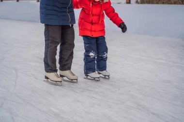 Genç bir anne, oğluna buz pateni pistinde buz pateni öğretiyor. Aile buz pateni sahasında kışın keyfini çıkarır.
