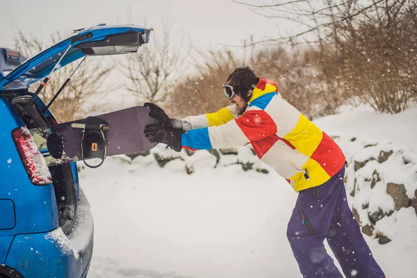 La tabla de snowboard no cabe en el coche. Un snowboarder está tratando de meter una tabla de snowboard en un coche. Humor, diversión —  Fotos de Stock