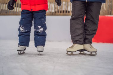 Genç bir anne, oğluna buz pateni pistinde buz pateni öğretiyor. Aile buz pateni sahasında kışın keyfini çıkarır.