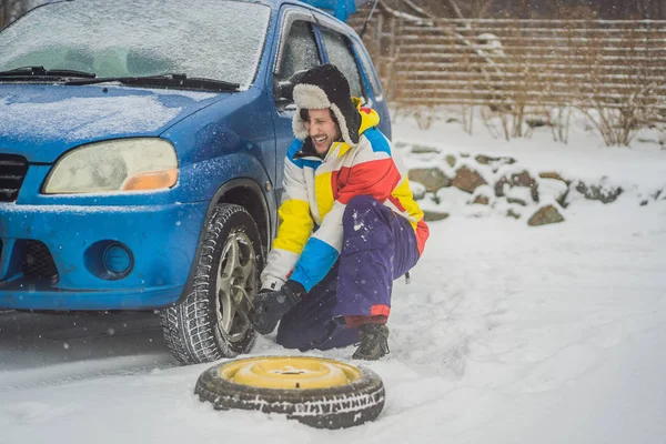 Accidente de invierno en la carretera. Un hombre cambia una rueda durante una nevada. Problemas de invierno —  Fotos de Stock