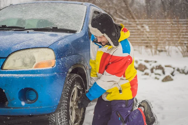 Winter accident on the road. A man changes a wheel during a snowfall. Winter problems — Stock Photo, Image
