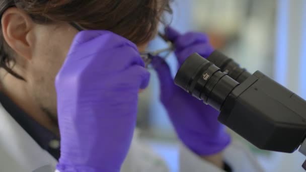Científico en un laboratorio utiliza un microscopio. Primer plano de tiro — Vídeo de stock