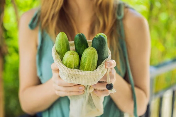 Komkommers in een herbruikbare zak in de handen van een jonge vrouw. Nul afvalconcept — Stockfoto