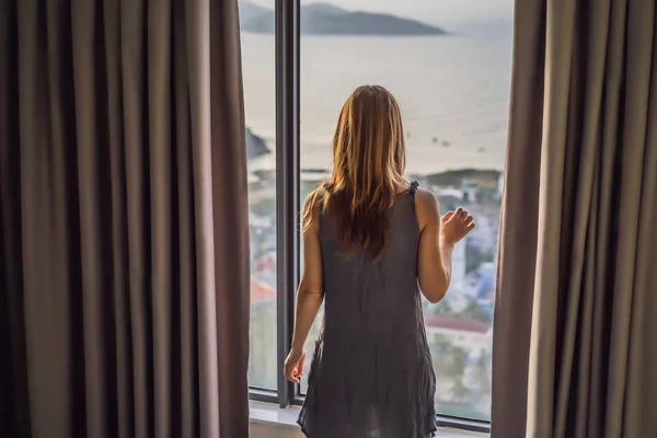 Молодая женщина открывает занавески на окне с видом на море — стоковое фото