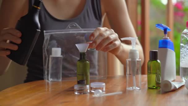 Jeune femme met ses cosmétiques et shampooing dans des bouteilles en plastique appropriées pour apporter à bord de l'avion. Trousse de voyage pour avion. Concept de voyage — Video